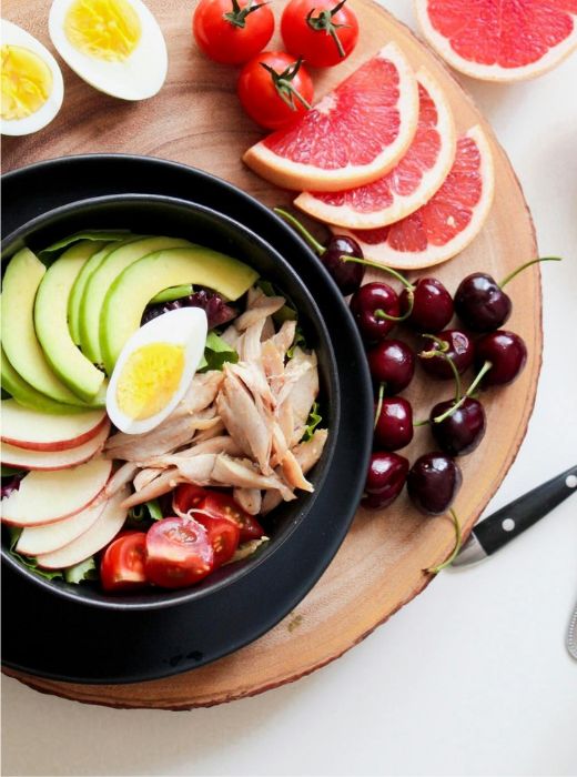 A colorful, healthy meal of grilled chicken, avocado, hard boiled eggs, and plenty of fruits and veggies